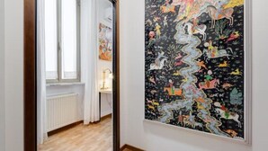 En gang med et stort abstrakt maleri på væggen og et vindue med hvide gardiner.