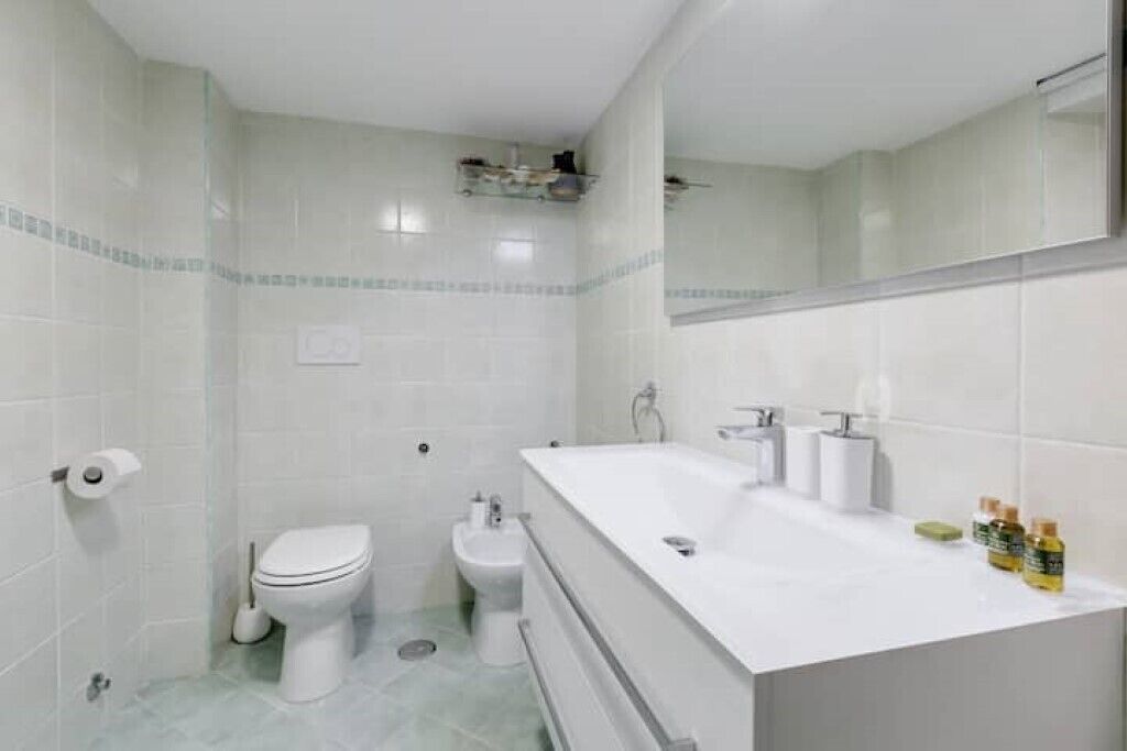A bathroom with a white toilet, bidet, and a large white sink with a mirror above it.