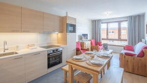 A modern kitchen with wooden cabinets, a built-in oven, and a dining area with a wooden table set for four. - 2-room apartment with parking in luxury residence in Alpe d'Huez (Huez)