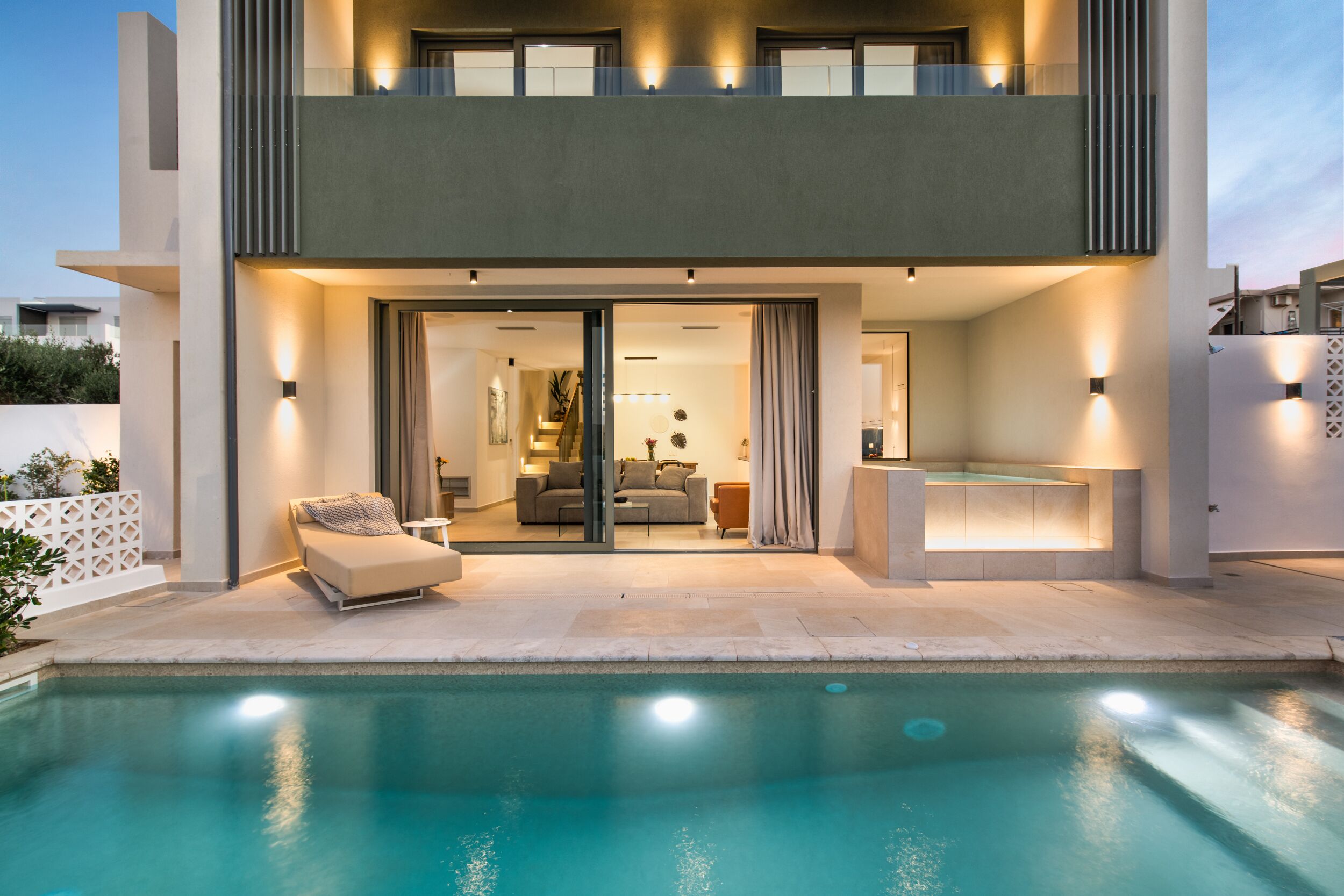 A modern two-story house with a swimming pool, a balcony, and a well-lit interior.