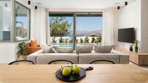 Ein modernes Wohnzimmer mit großem Fenster, einer Couch, einem Esstisch mit Äpfeln und einem Fernseher.