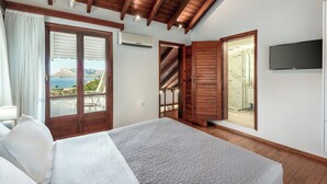 Ein Schlafzimmer mit einem großen Bett, Holzbalkendecke, einem Fernseher und Meerblick.