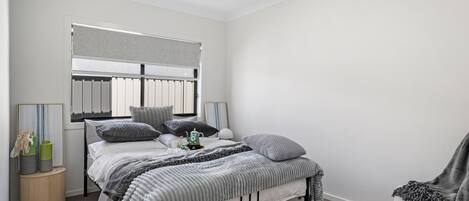Un dormitorio con cama, mesitas de noche, una silla y una ventana con persianas.