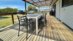 Een overdekt terras buiten met een tafel, stoelen, een barbecue en uitzicht op de omgeving.