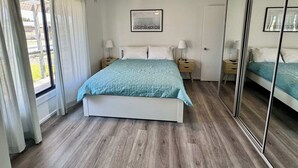 Een slaapkamer met een bed, een plafondventilator, een nachtkastje, een spiegel en een raam met gordijnen.