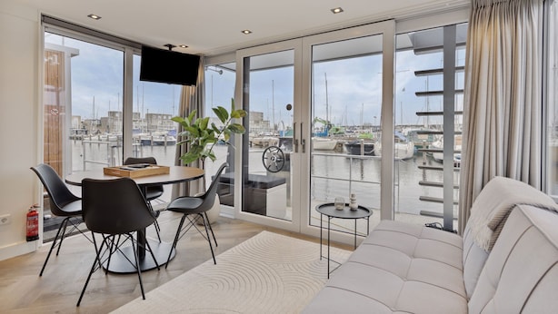 Ein modernes Wohnzimmer mit Essbereich, großen Schiebeglasfenstern, einem Flachbildfernseher und Blick auf eine Marina.