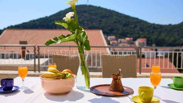 Un tavolo con una ciotola di frutta, un vaso di fiori e due bicchieri di succo d'arancia.