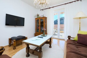 A living room with a flat-screen TV, a wooden cabinet, a sofa, and a table with a remote control.