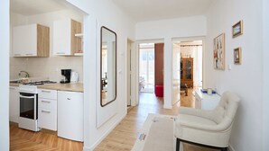 Una cucina moderna con mobili bianchi, forno a incasso e macchina da caffè. C'è un grande specchio sulla parete e una sedia nella zona pranzo.