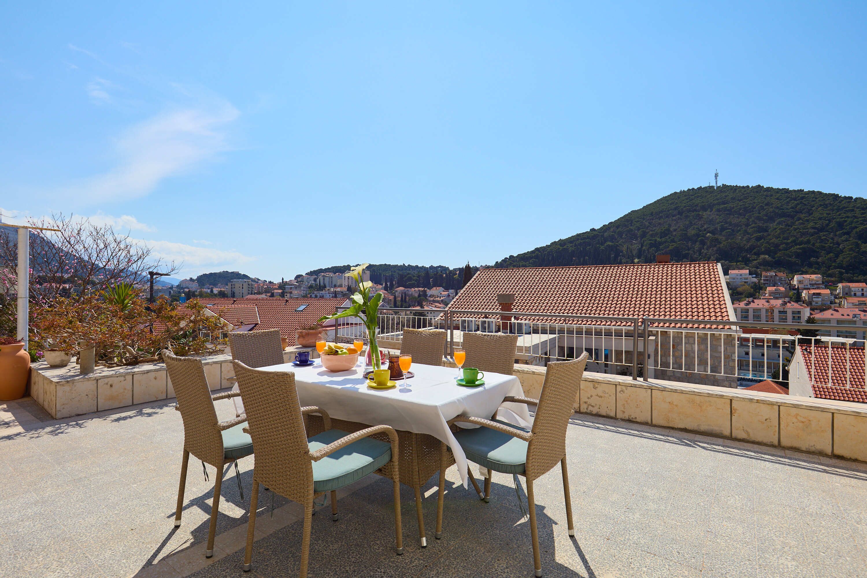 Une terrasse avec une table dressée pour le dîner, offrant une vue sur un paysage urbain avec des bâtiments aux toits rouges et une colline.