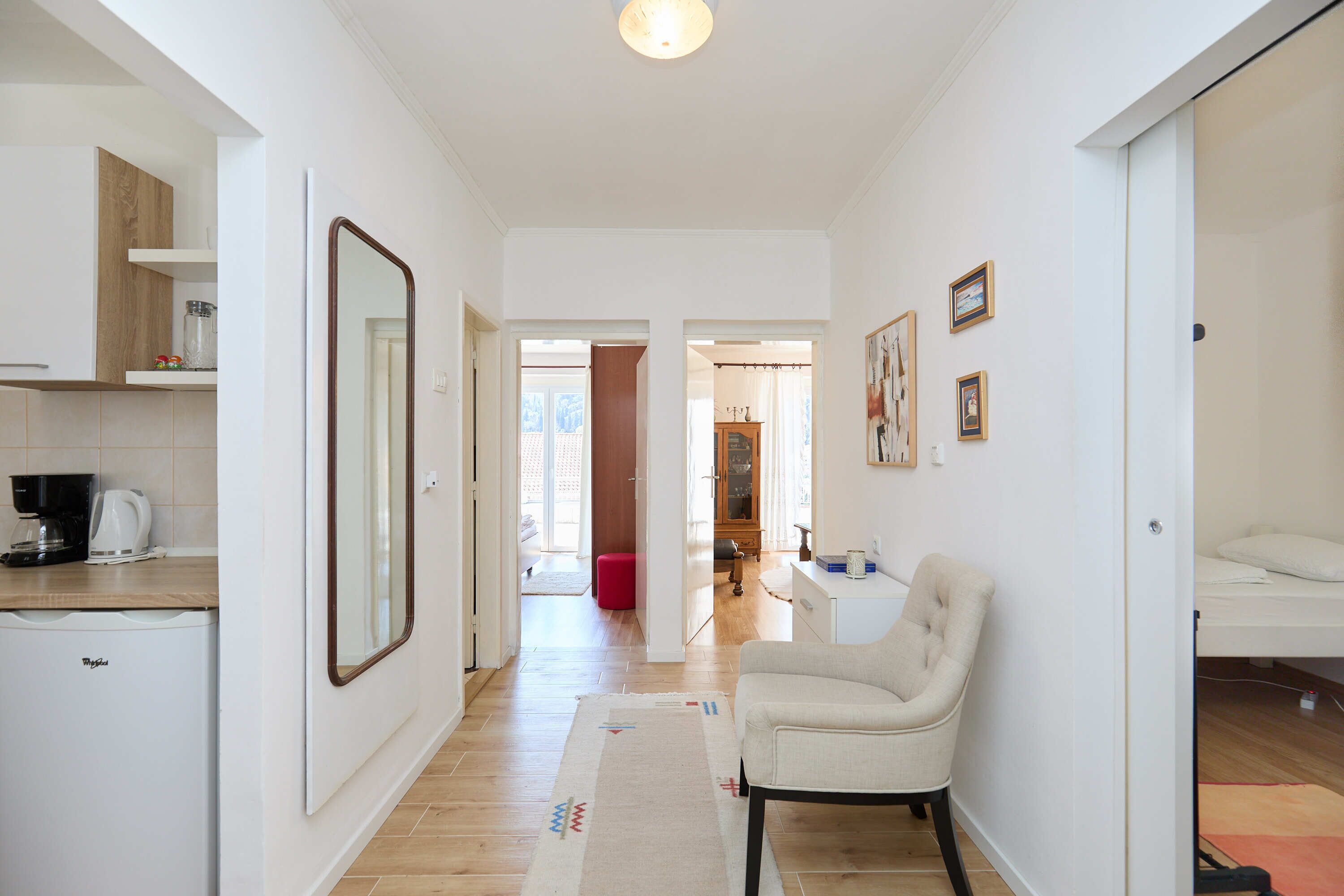 A modern, well-lit hallway with a compact kitchen area, a seating area with a chair, and a bed in the background.