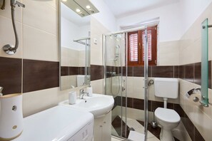 A bathroom with a glass-enclosed shower, a white sink, and a toilet.
