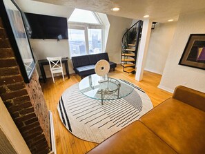 Un salon moderne avec une table basse en verre, un canapé noir, un fauteuil blanc et un escalier en colimaçon.
