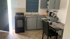 A compact kitchen with a gas stove, sink, and a small dining area with a chair and table. - 1 Bed Studio Apt - Parking, Wifi, Mountain Views (Scarborough)