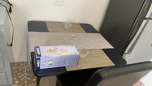 A small dining area with a table set for two, a box of Conair hair dryer, and a wine glass. - 1 Bed Studio Apt - Parking, Wifi, Mountain Views (Scarborough)