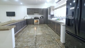 Uma cozinha moderna com bancadas de granito, armários escuros, forno embutido, geladeira e ventilador de teto.