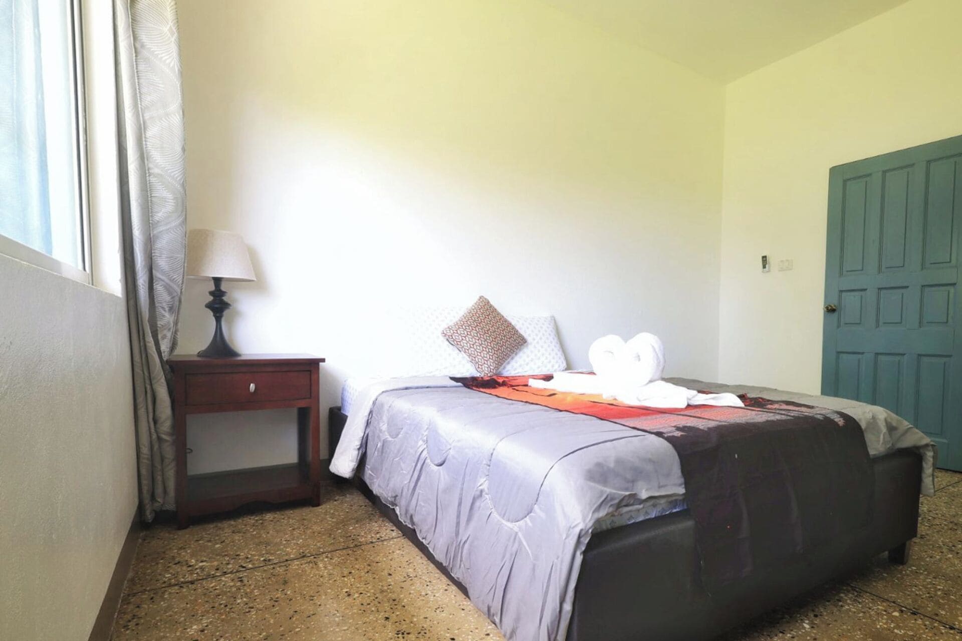 A bedroom with a bed, a nightstand, a lamp, and a door.