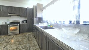 Uma cozinha com armários de madeira escura, forno de aço inoxidável, micro-ondas e uma janela grande com cortinas.