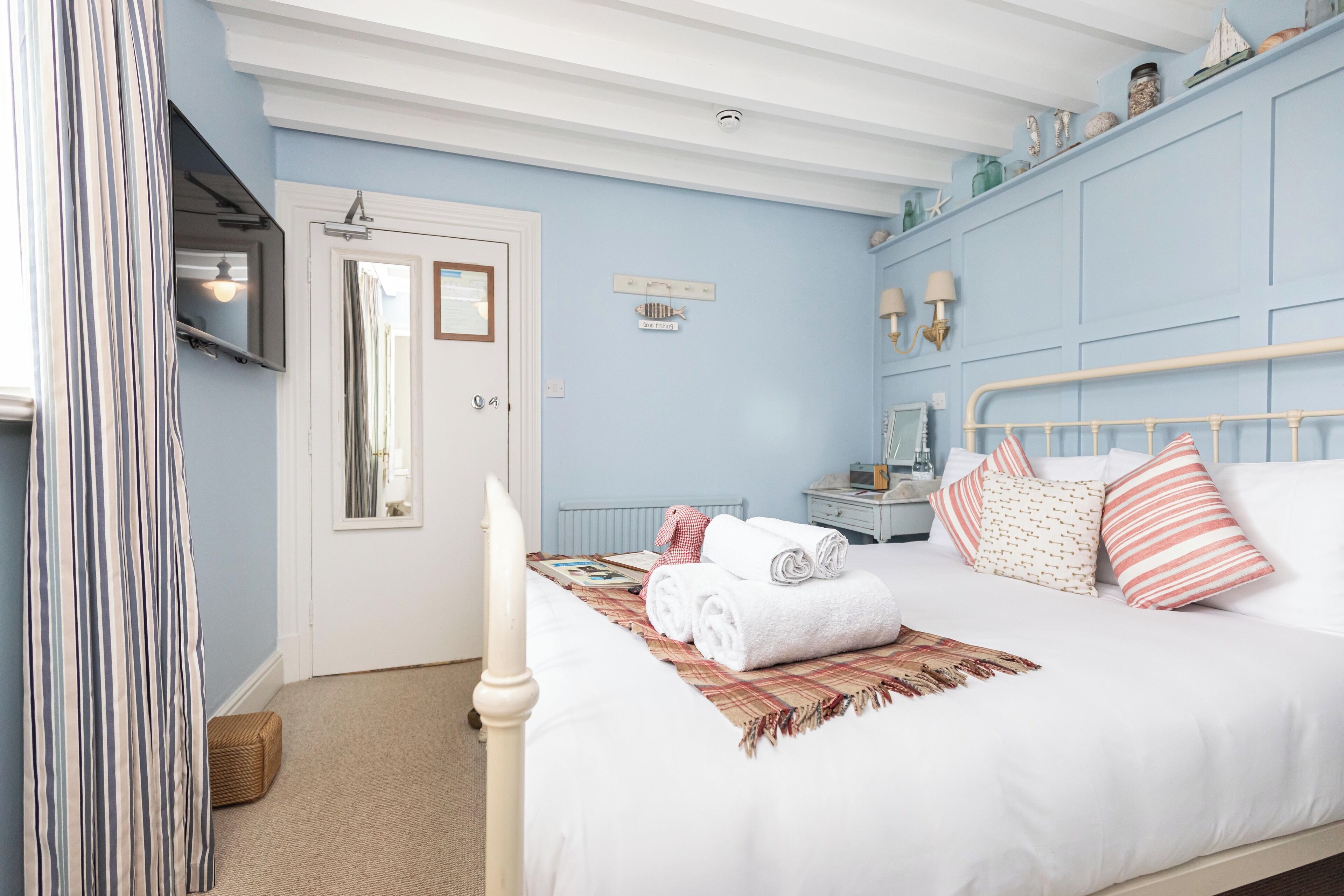A bedroom with a bed, a bedside table, a mirror, and a window with curtains.