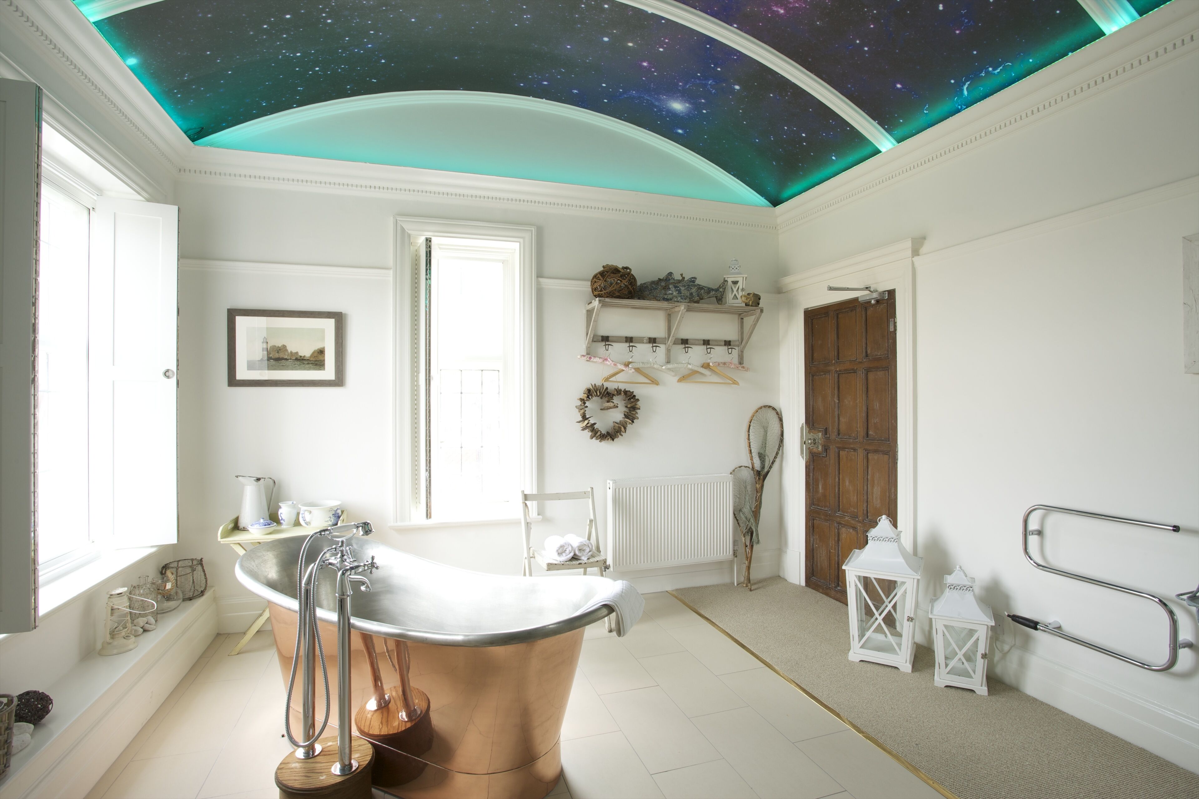 A bathroom with a starry ceiling, a copper bathtub, a white sink, and a wooden door.