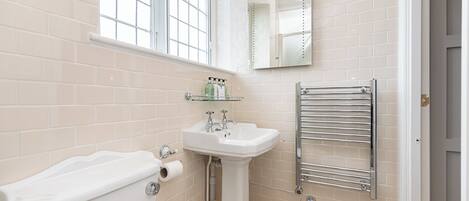 Une salle de bain avec un lavabo blanc, une étagère en verre où sont rangés les articles de toilette, des toilettes et un porte-serviettes.