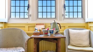 A room with three windows, wicker chairs, a small table with various items, and a yellow wall. - The Beach House (Lymington)