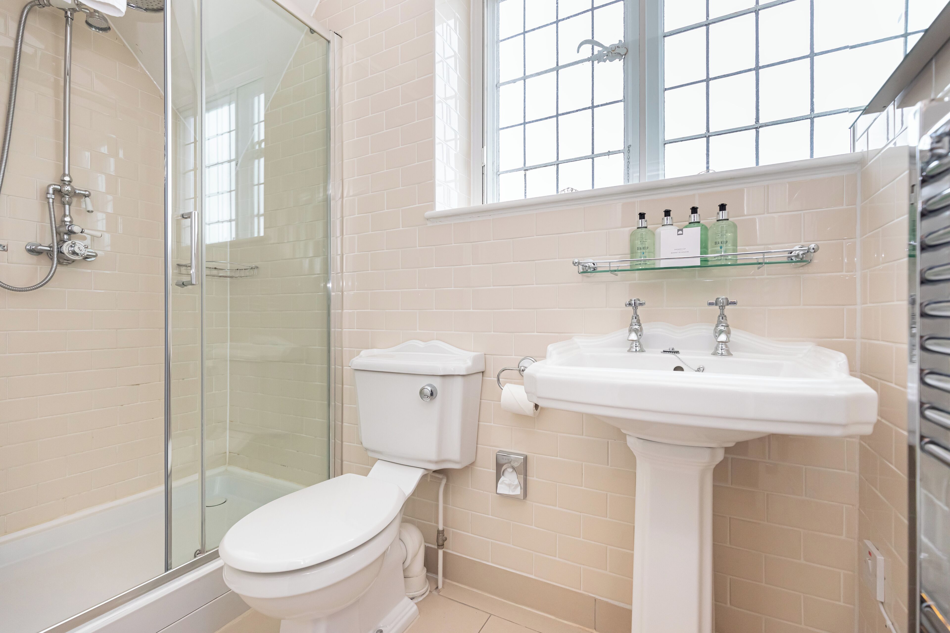 A bathroom with a glass shower enclosure, a toilet, a sink, and a window above the sink.