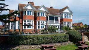 A large, two-story building with a brick facade and white trim, featuring multiple windows and a balcony. - The Beach House (Lymington)