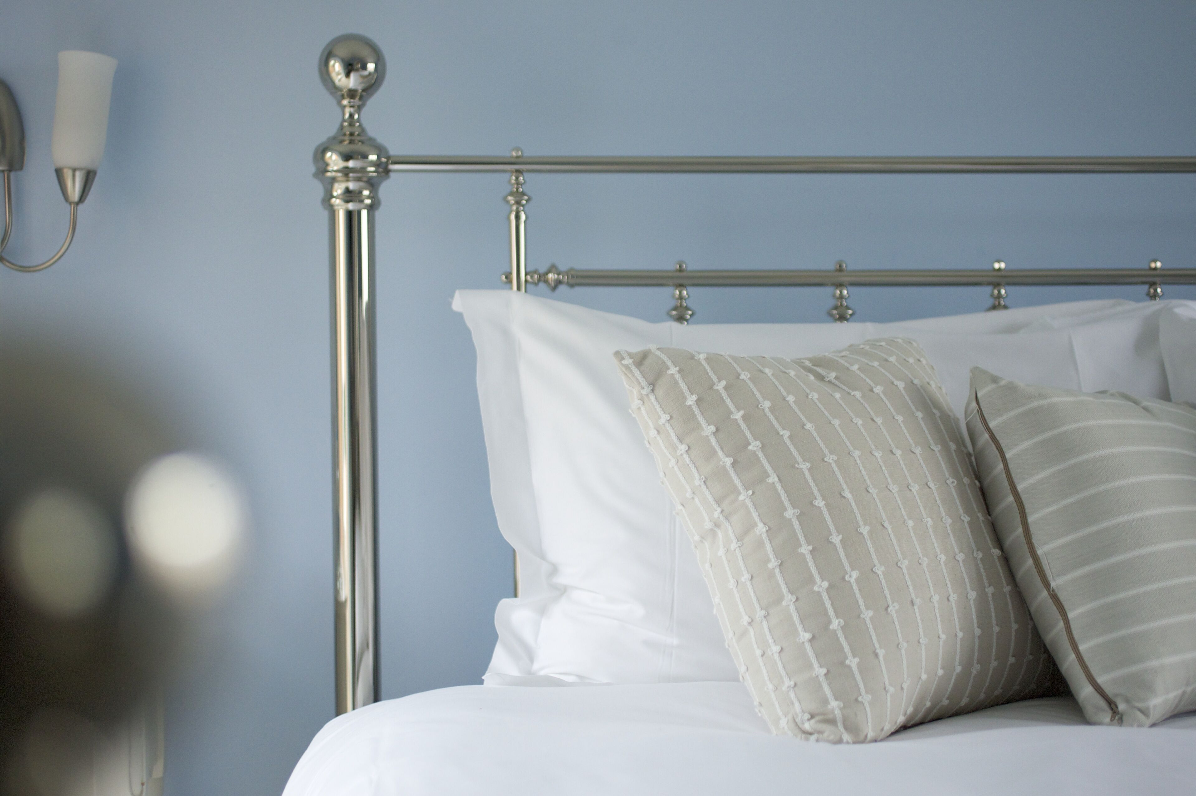 Una cama con estructura metálica, ropa de cama blanca y almohadas a rayas.