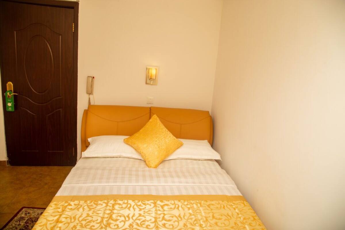Une chambre d’hôtel avec un lit, une porte en bois, une lampe fixée au mur et un téléphone.