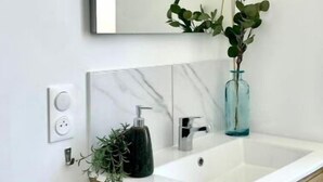 A bathroom with a white sink, a mirror, and a wooden vanity. - Chez Clément et Mathilde - Studio Hyper Centre (Saint-Amand-les-Eaux)