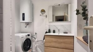 A compact, modern bathroom with a built-in washer and dryer, a wooden vanity, and a large mirror above the sink. - Chez Clément et Mathilde - Studio Hyper Centre (Saint-Amand-les-Eaux)