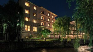 A multi-story hotel with illuminated windows, a stone wall, and a water feature in front.
