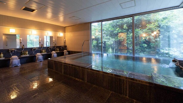A modern spa with a large glass-enclosed hot tub, multiple sinks, and a view of lush greenery outside. - Tokyu Vacations Izukogen (Ito)