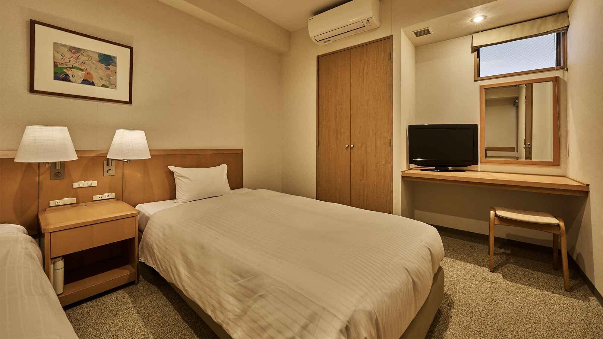 A hotel room with a bed, bedside lamps, a desk with a television, a wardrobe, and a framed picture on the wall.