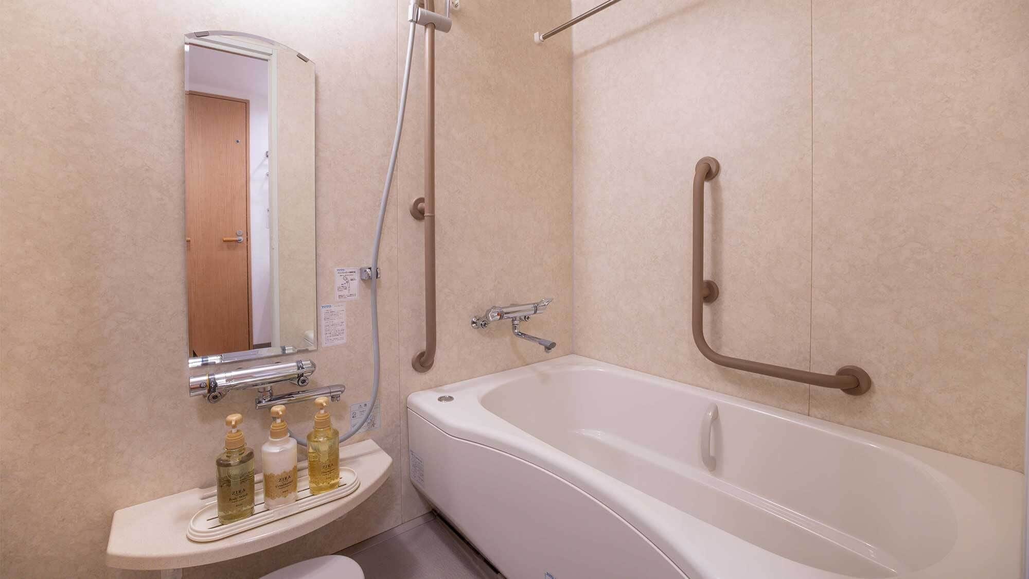 Un bagno con una vasca da bagno bianca, un lavandino con tre flaconi di sapone liquido e uno specchio.