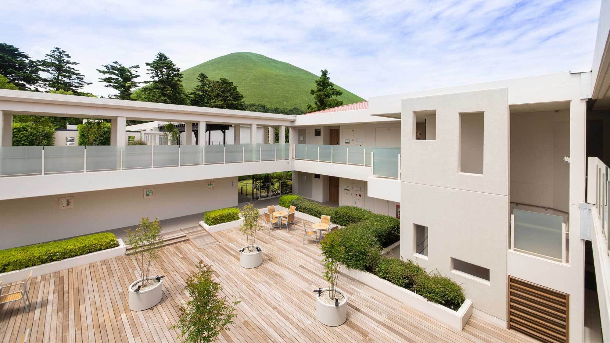 A modern building with a wooden deck, outdoor seating, and a mountain view.