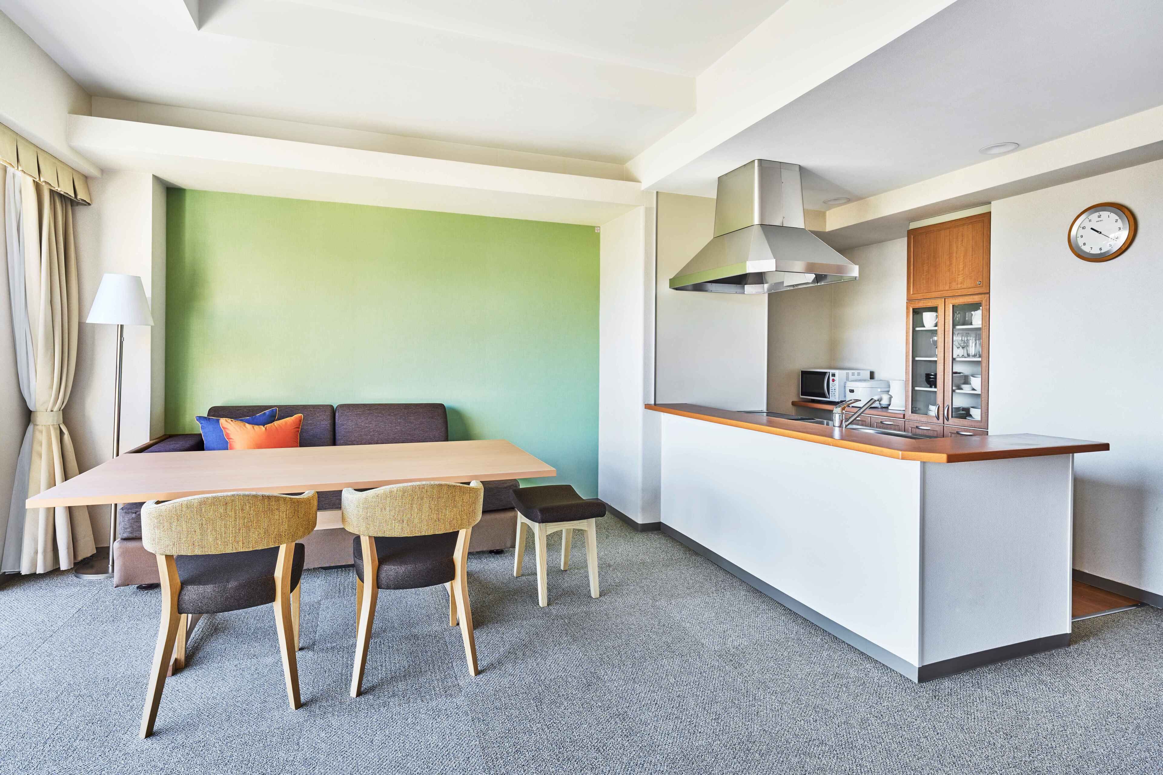 A modern hotel room with a dining area, a kitchenette, and a green accent wall.