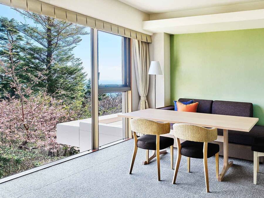 Una habitación moderna con un ventanal grande, una mesa de comedor, dos sillas, un sofá y una lámpara.