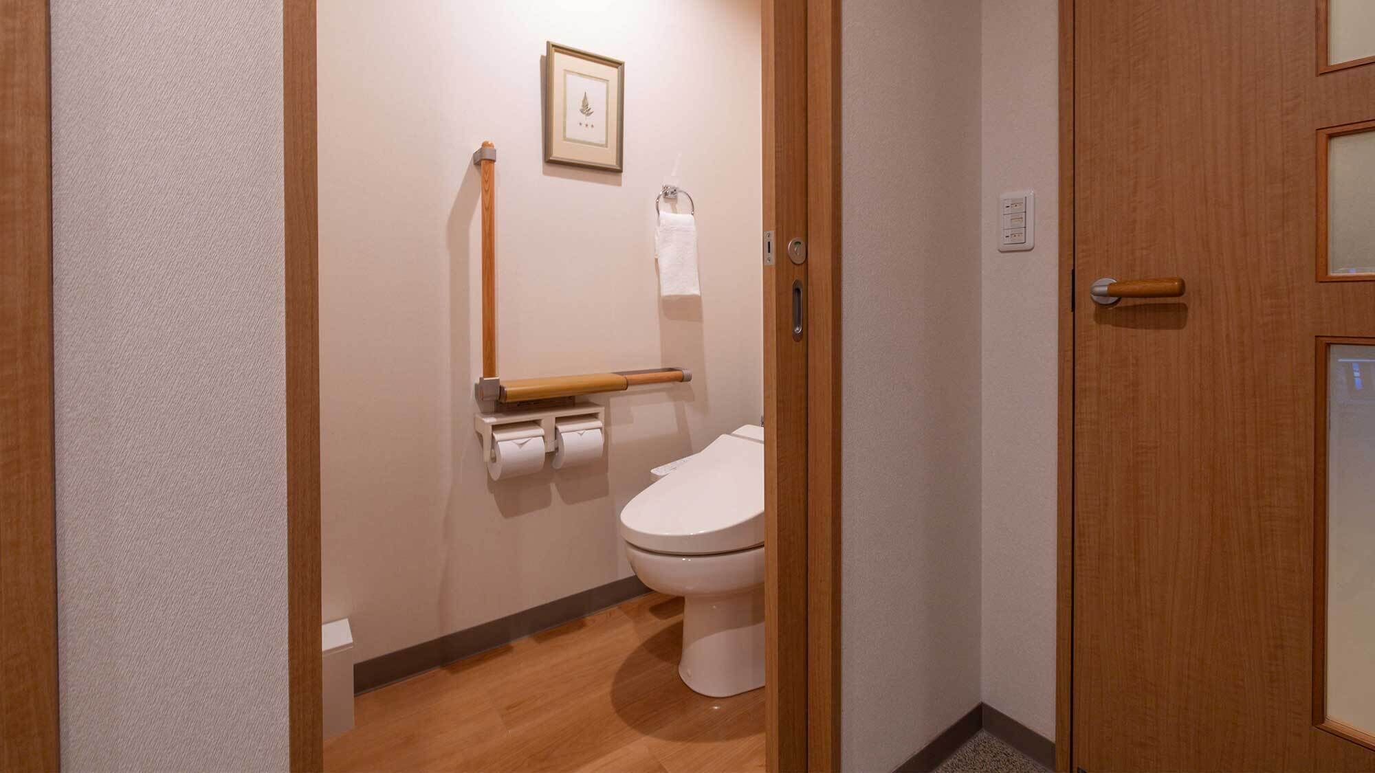 A small, clean bathroom with a toilet, a wooden toilet paper holder, a framed picture on the wall, and a towel hanging on a rack.