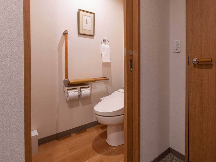 A small, clean bathroom with a toilet, a wooden toilet paper holder, a framed picture on the wall, and a towel hanging on a rack.
