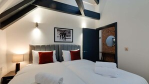 A hotel room with a large bed, a headboard, a nightstand with a lamp, a framed picture on the wall, a door with a mirror, and exposed wooden beams on the ceiling. - Harrisons Aparthotel (Liverpool)