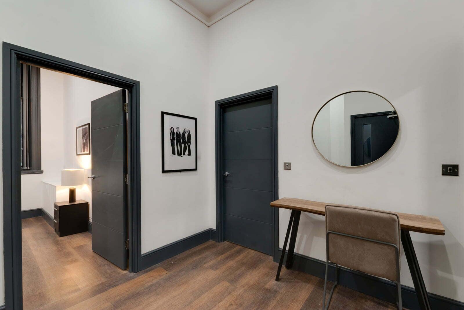 Ein Flur mit einer dunklen Tür, einem gerahmten Bild an der Wand, einem runden Spiegel und einem kleinen Tisch mit einem Stuhl.
