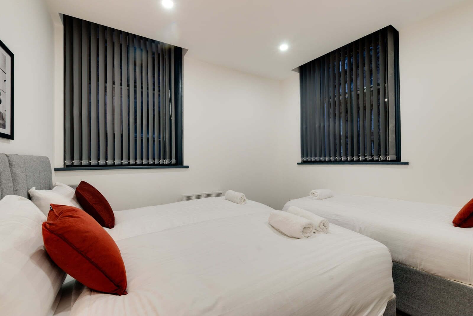 Ein Hotelzimmer mit zwei Betten, jeweils mit weißer Bettwäsche und roten Kissen, sowie einem grauen Sofa.