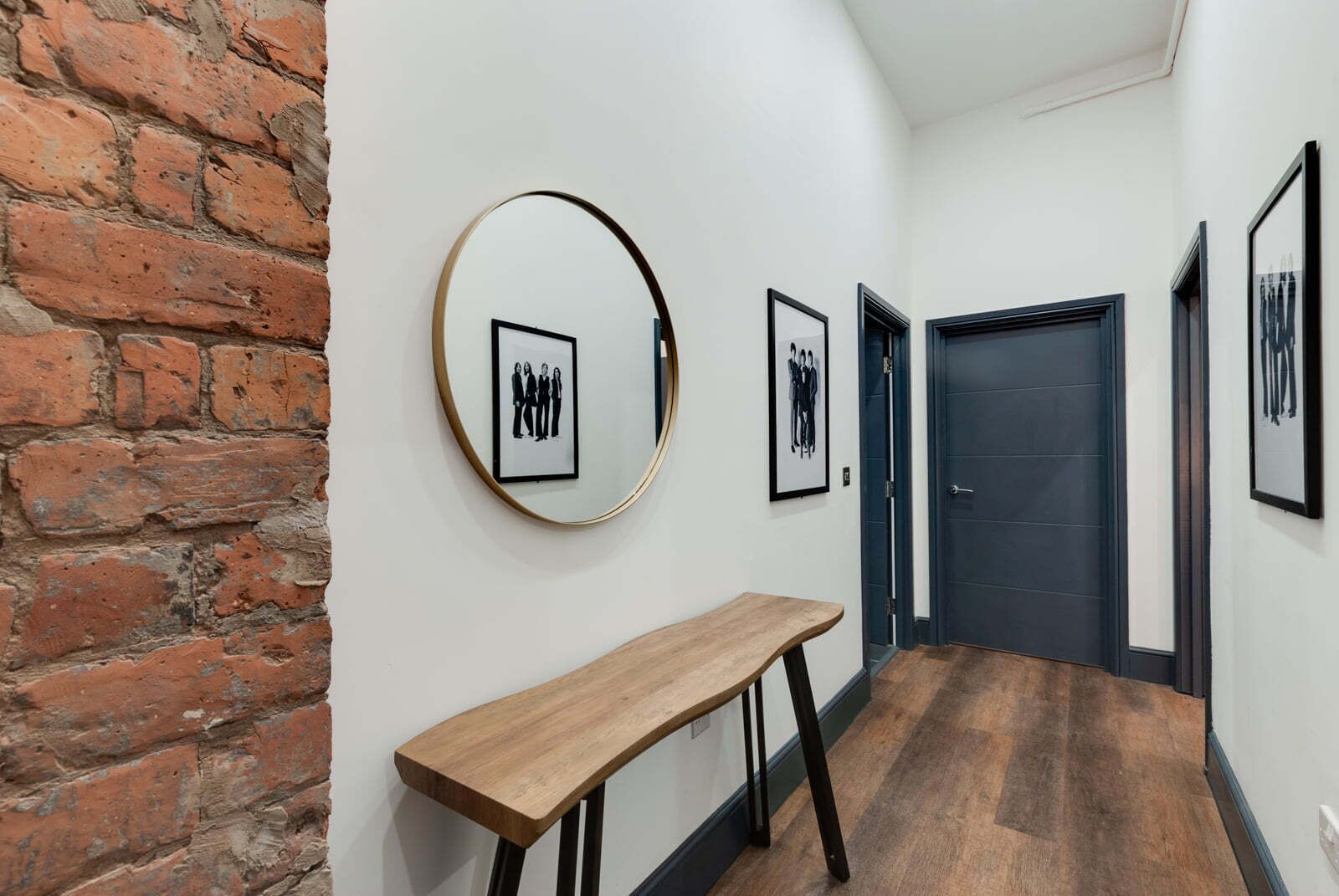 A hallway with a brick wall, a round mirror, and framed pictures on the wall.