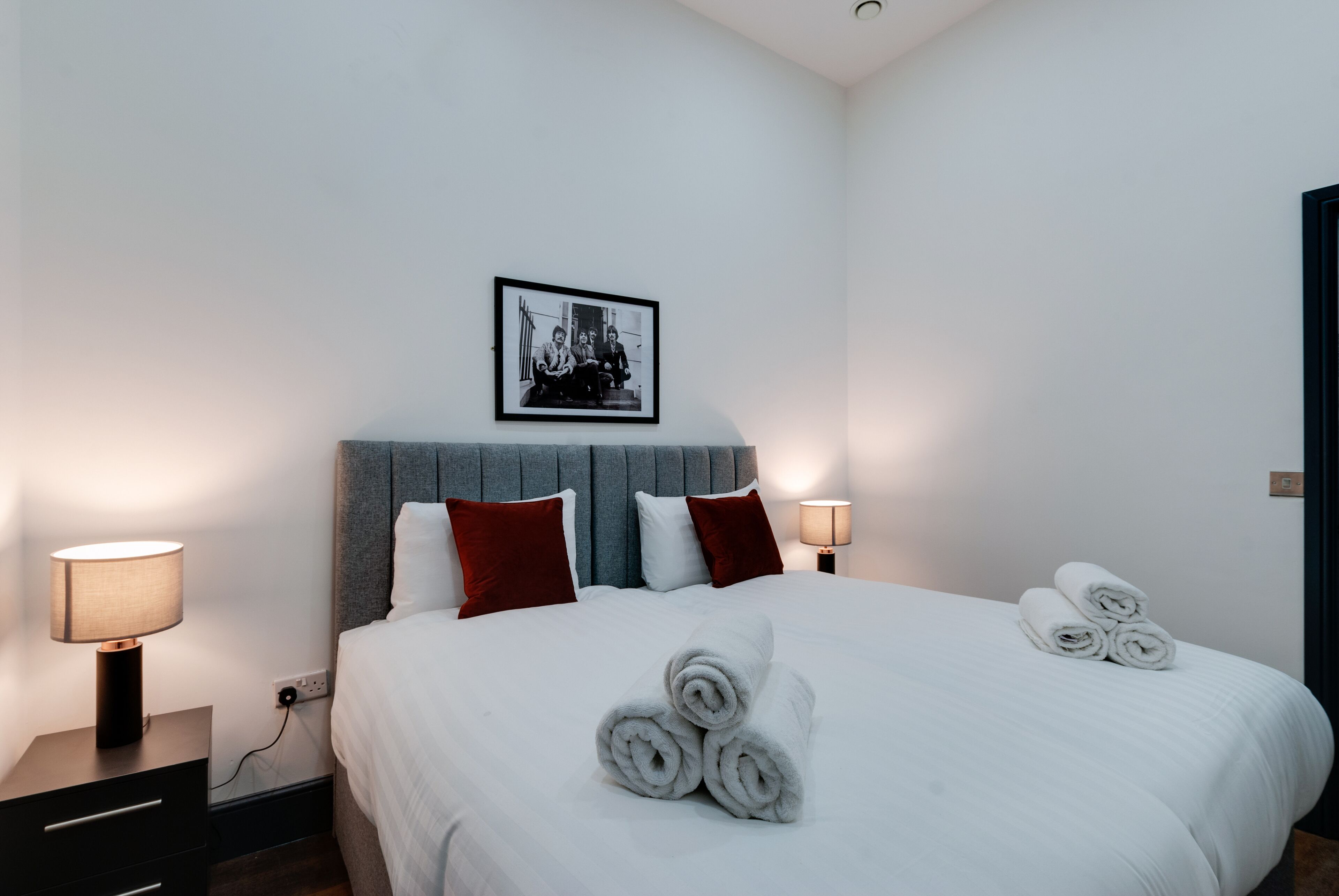 A neatly made bed with rolled towels, a headboard, and two bedside lamps.