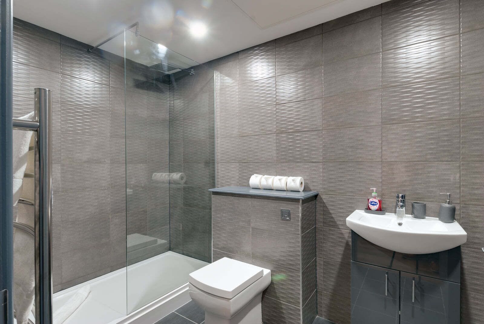 A modern bathroom with a glass shower enclosure, a toilet, and a sink with toiletries.
