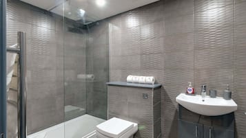 A modern bathroom with a glass shower enclosure, a toilet, and a sink with toiletries.