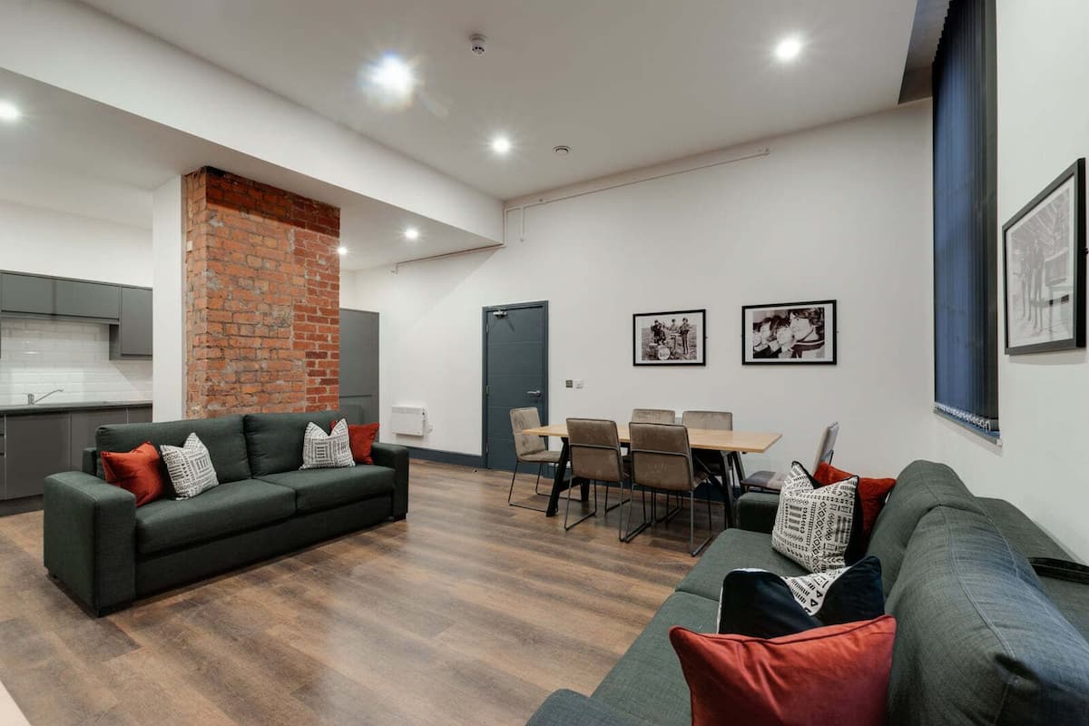 A modern living room with a dining area, a kitchen, and a brick accent wall.
