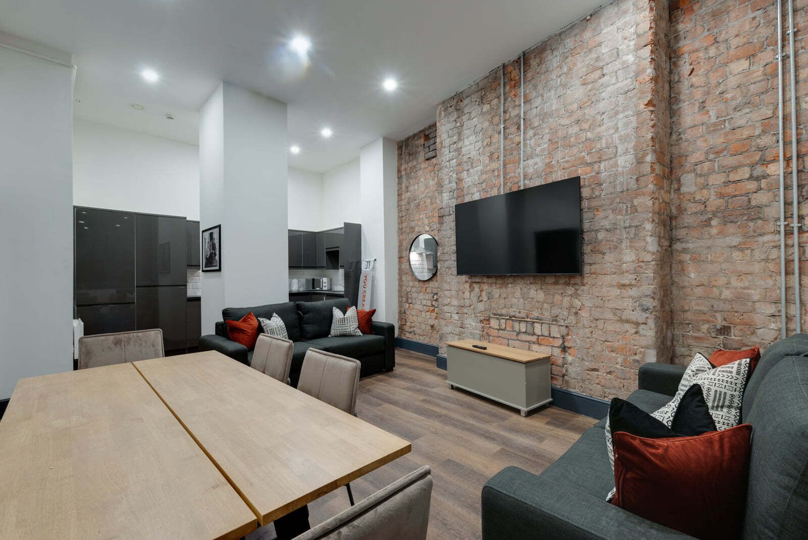A modern living room with a brick wall, a flat-screen TV, and a dining area.